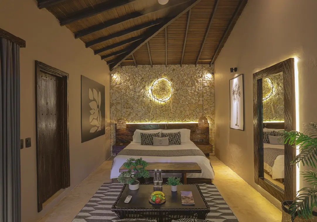 King bed in a tropical-themed hotel room with a stone accent wall, warm lighting, and wooden ceiling beams.